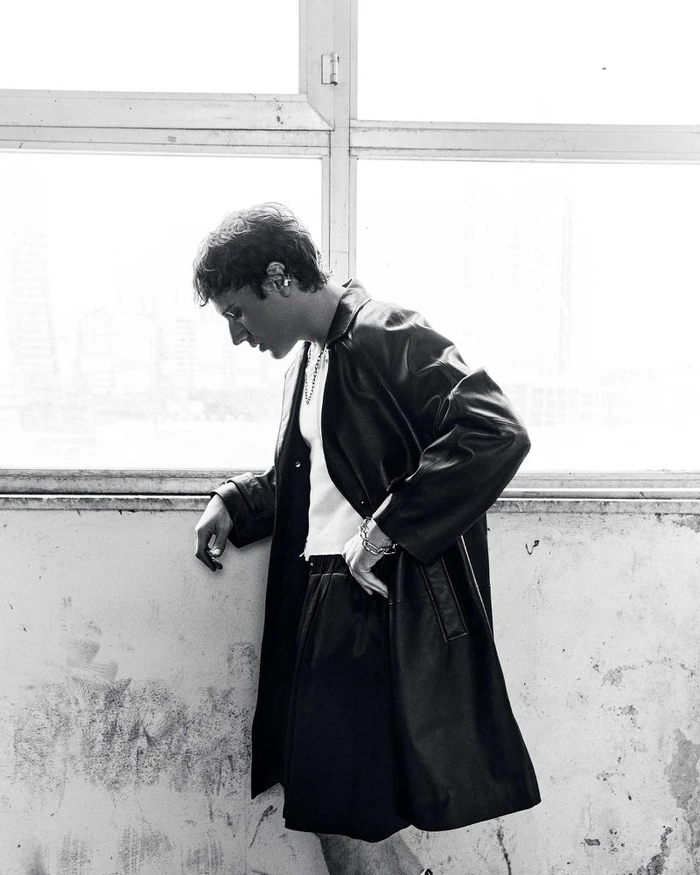 Man wearing a black leather coat and shorts standing near a large window for a Vogue Turkey editorial