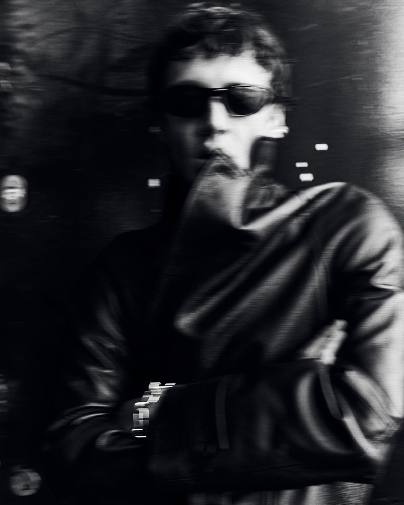 Monochrome portrait of a man in sunglasses wearing a dark leather jacket with crossed arms