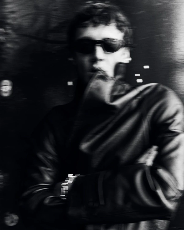 Monochrome portrait of a man in sunglasses wearing a dark leather jacket with crossed arms