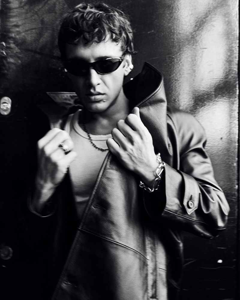 Monochrome portrait of a man wearing dark sunglasses, a white tank top, and a leather coat, captured for Vogue Turkey.
