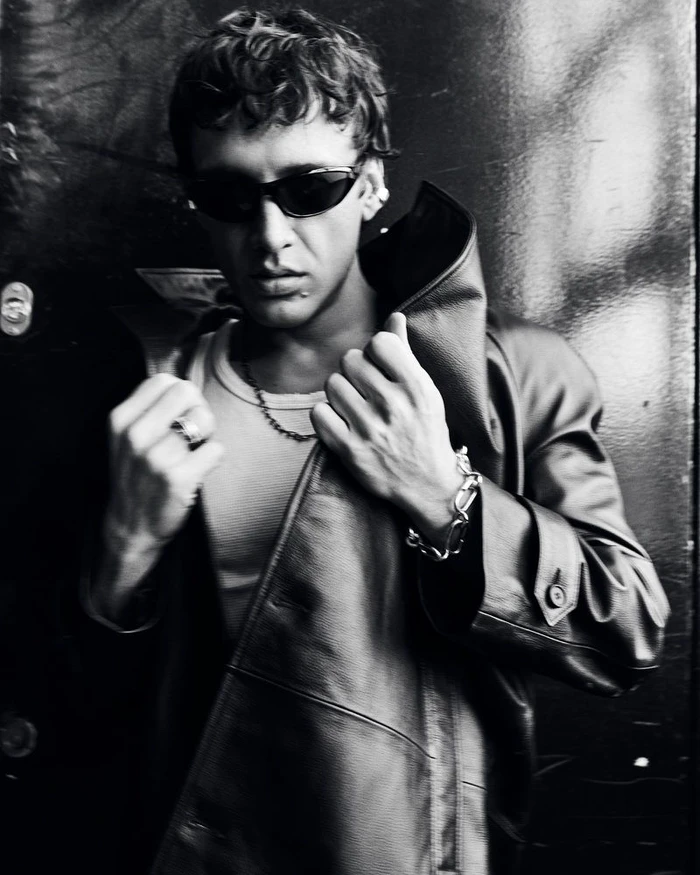 Monochrome portrait of a man wearing dark sunglasses, a white tank top, and a leather coat, captured for Vogue Turkey.