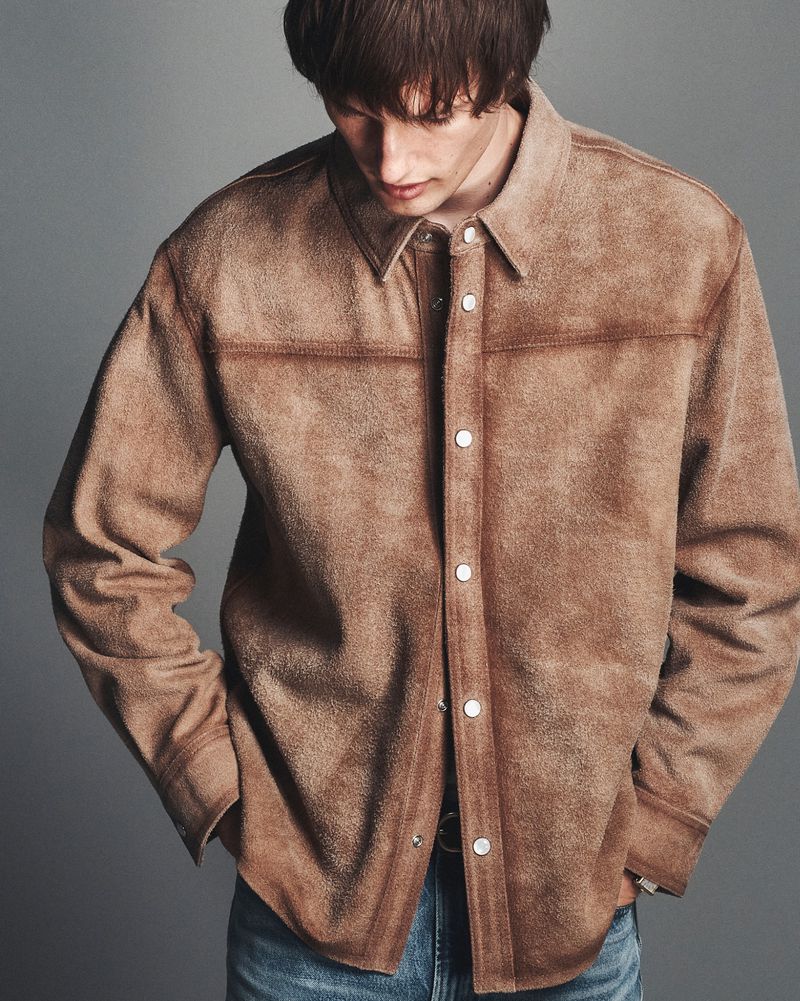 Model Thatcher Thornton wearing a brown suede snap-front overshirt and blue denim jeans against a grey studio backdrop.