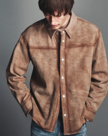 Model Thatcher Thornton wearing a brown suede snap-front overshirt and blue denim jeans against a grey studio backdrop.