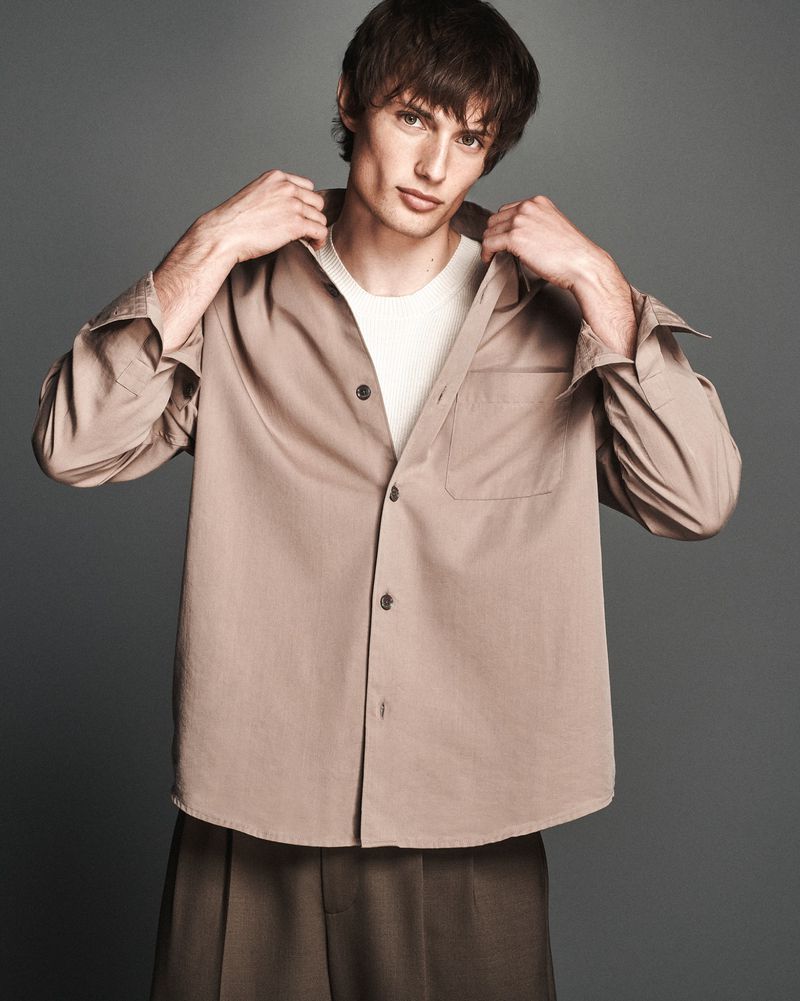 Model Thatcher Thornton posing in a taupe button-up overshirt and white t-shirt against a seamless grey studio background.