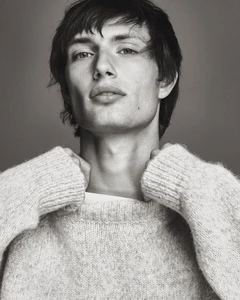 Thatcher Thornton wearing a textured light grey knit sweater looking at the camera against a grey studio backdrop.