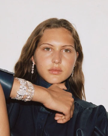 Angelina Kendall resting her hand near her chin, wearing diamond cuff bracelets, drop earrings, and a dark navy leather collared shirt.