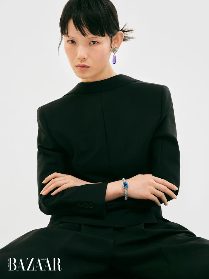 Model Xie Chaoyu in a black tailored jacket, purple drop earring, and blue gemstone bracelet against a white seamless background.