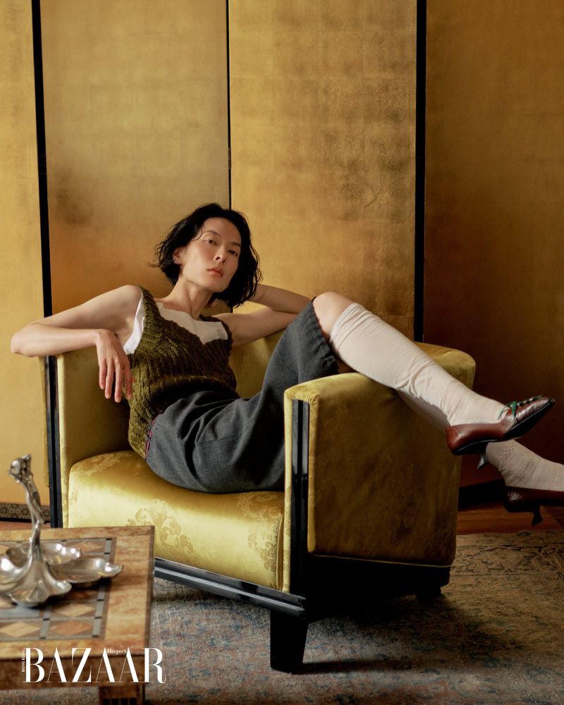 Model Hsin-Yu Liu relaxing in a yellow-green velvet armchair against a golden folding screen for Harper's Bazaar Hong Kong.