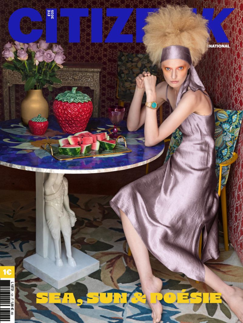 Magazine cover featuring a model seated at a table with watermelon slices, flowers, and decorative items in a patterned interior setting.