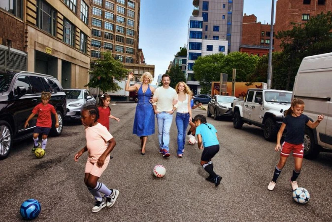 Hannah Waddingham, Jason Sudeikis, and Juno Temple walking on an urban street surrounded by kids playing soccer.
