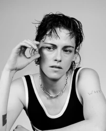 Black and white portrait of Kristen Stewart wearing a black tank top with white trim and a silver chain necklace.