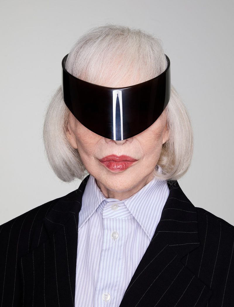 Elegant elderly woman in futuristic visor and business attire, capturing a blend of sophistication and avant-garde style, studio lit.