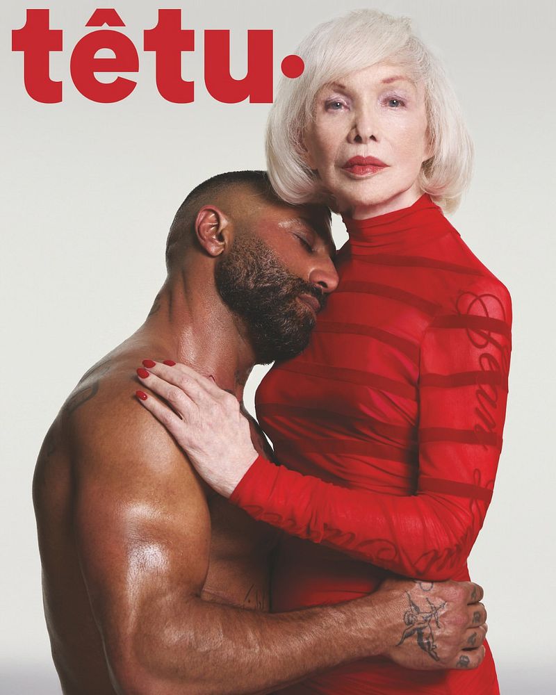 Magazine cover featuring an adult woman in a red dress embracing a muscular, bare-chested adult man, against a light gray background.