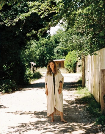 Model Nataša Vojnović standing barefoot on a sunlit dirt path wearing an off-white draped kaftan for Vogue Adria.