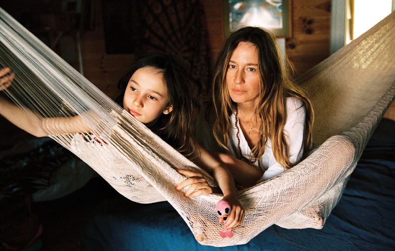 Model Nataša Vojnović and a young girl resting together in a woven cream hammock indoors over a blue bed.