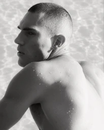 Black and white profile of a shirtless man with water droplets on his back looking away against rippling water.