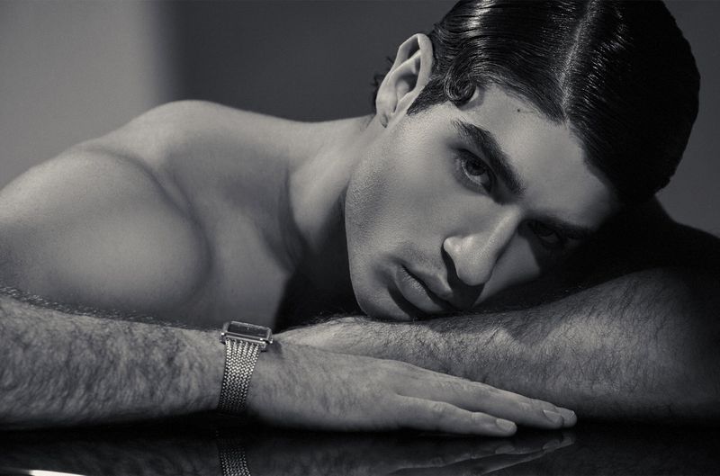 Close-up portrait of a man resting head on arms wearing a silver wristwatch in black and white