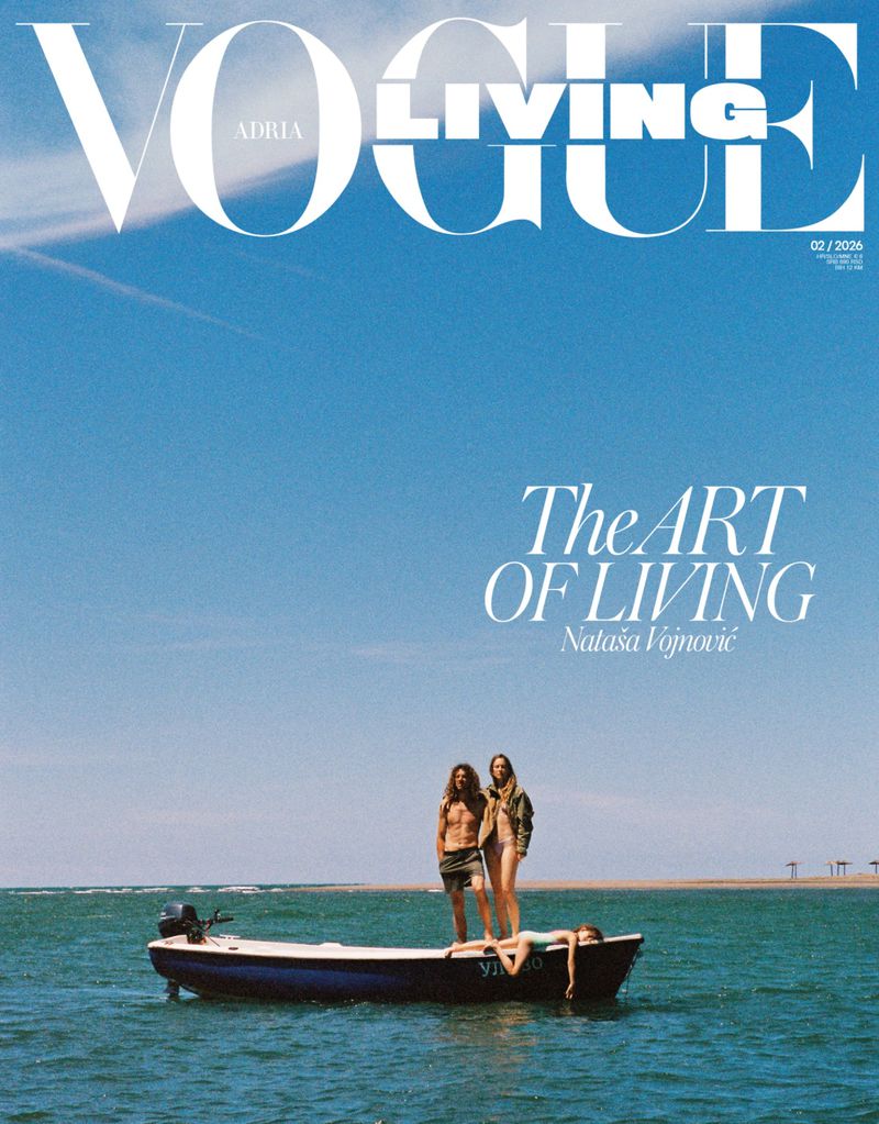 Three models standing and lying on a small boat floating on clear blue ocean water under a clear sky.