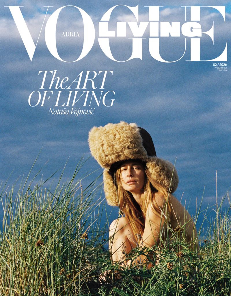 Model Nataša Vojnović wearing a fluffy faux fur ushanka hat amidst tall grass under an overcast sky for Vogue Adria