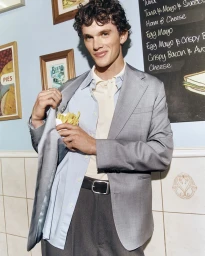 Young man wearing a grey blazer, blue shirt, and holding fries inside his jacket pocket in a cafe.
