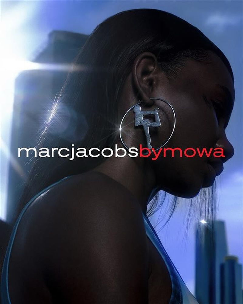Fashion portrait of an African-descent adult female with large hoop earrings, city skyline background, and 'Marc Jacobs by Mowa' text overlay.