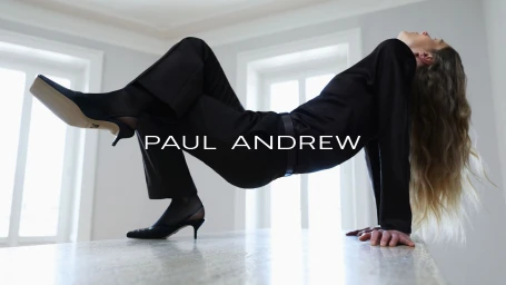 Model Laura Morgan arches backward on a stone surface wearing a black tailored outfit and Paul Andrew black slingback pumps.