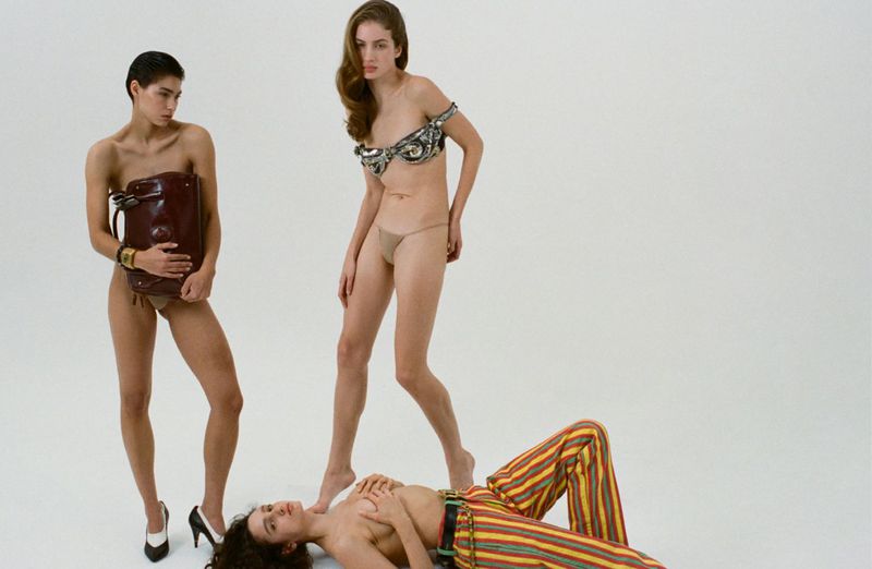 Three models posing against a white studio seamless backdrop, featuring striped trousers and a structured brown leather handbag.