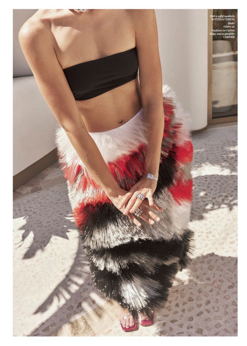 High-angle view of a woman wearing a black bandeau top and a tiered red, black, and white feathered skirt on a sunlit terrace.