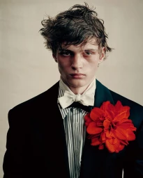 Model Artjom Zagrebaylov wearing a black jacket, striped shirt, cream bow tie, and a large red flower pinned to his lapel.