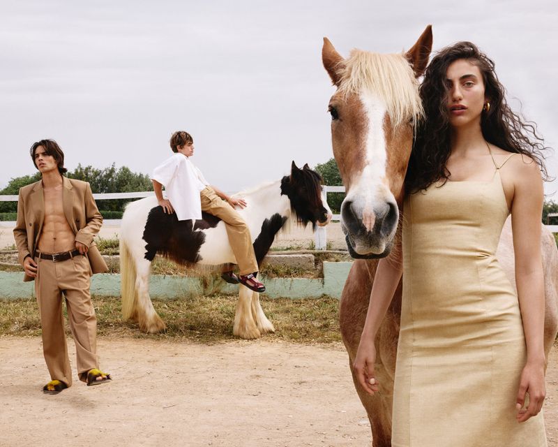 Fashion editorial shot with an adult female posing with a horse, a young child sitting on a horse, and an adult male in a tan suit.