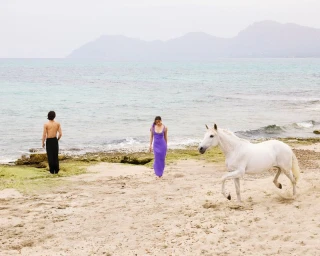 Models and a white horse on a sandy beach near the ocean for Venroy Mallorca 2025 campaign by Kito Muñoz