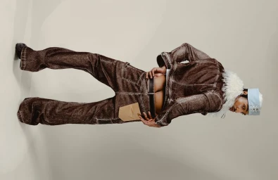 Model Laro Junior posing from behind in a brown denim jacket with fur trim and matching flared trousers against a studio backdrop.