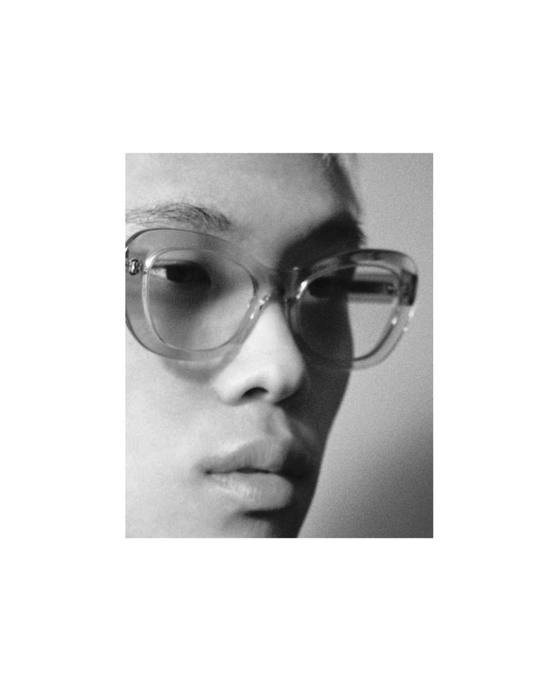 Close-up portrait of a model wearing thick translucent eyeglasses against a plain background