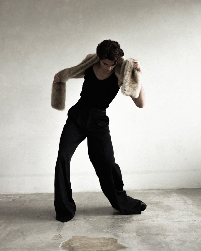 William Franklyn-Miller wearing a black tank top and dark trousers with a faux fur stole in Numero Netherlands editorial photography.