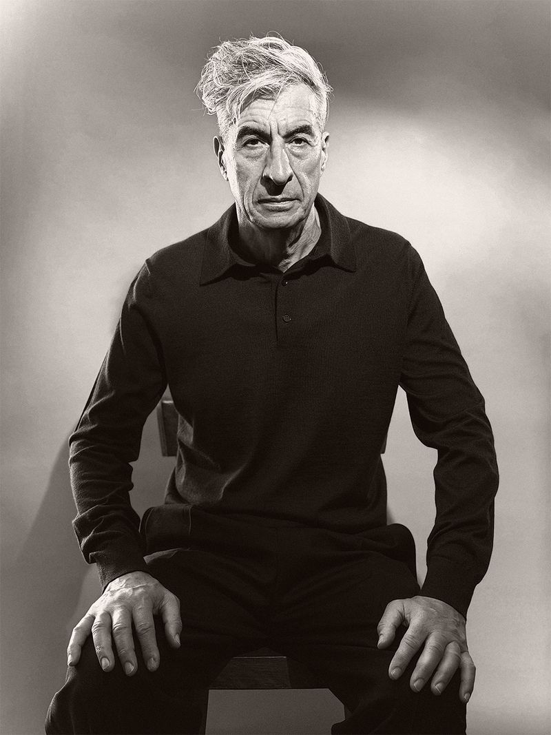Portrait of older man wearing black polo shirt sitting against gradient background for U Repubblica by Paul Kooiker