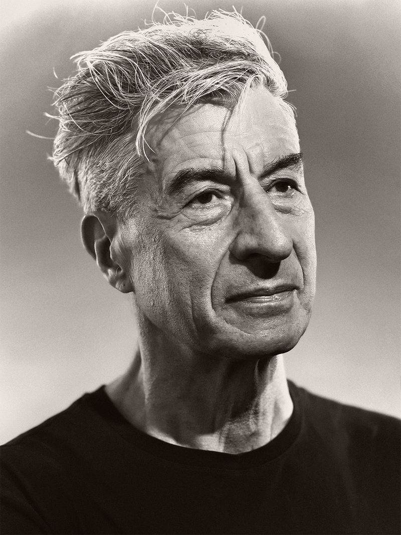Close-up monochrome portrait of artist Maurizio Cattelan looking to the side in a black crew neck t-shirt.