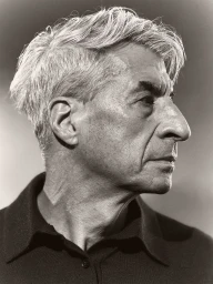 Profile portrait of artist Maurizio Cattelan in a dark collared shirt against a neutral studio backdrop.
