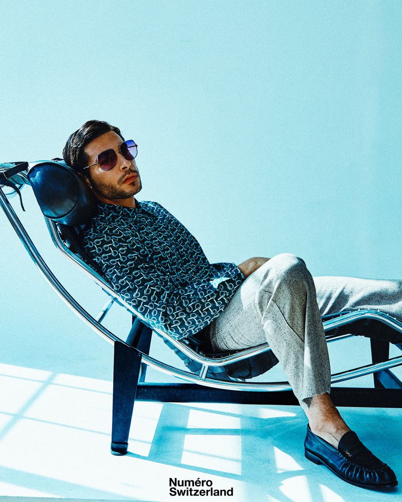 Model Andrea Denver reclining on a chaise lounge wearing sunglasses and a patterned shirt for Numéro Switzerland.