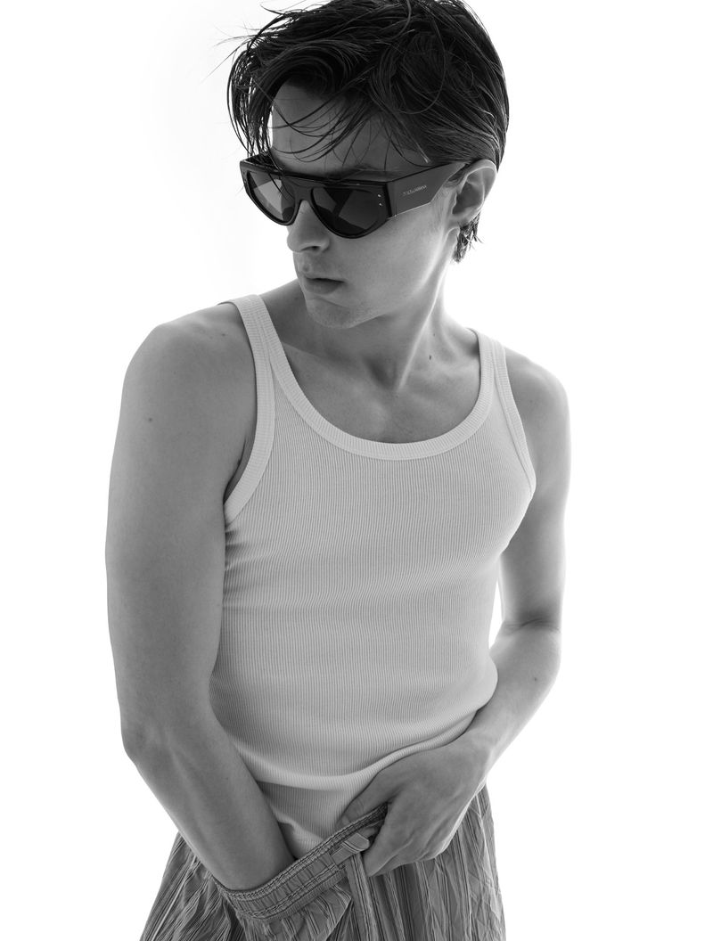 Man wearing dark sunglasses and a white ribbed tank top against a bright background for L'Officiel Hommes Turkey.