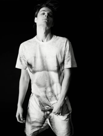 Corey Fogelmanis poses in a graphic trompe-l'œil print t-shirt and matching shorts against a black backdrop.