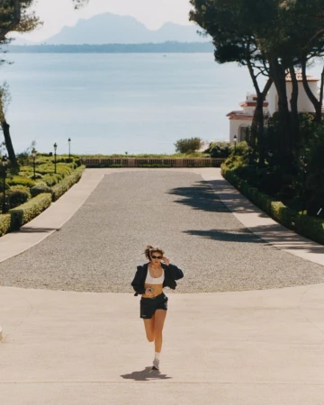 Olivia Aarnio running in a white sports bra and dark shorts along a paved path overlooking the sea.
