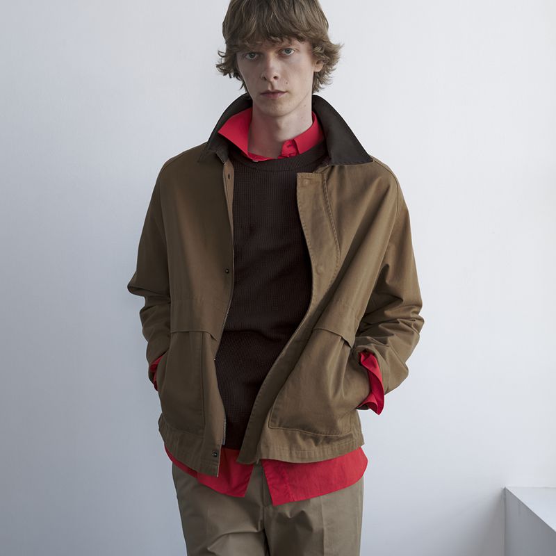 Model Guus Bracke posing in a brown jacket layered over a bright red collared shirt against a white backdrop.