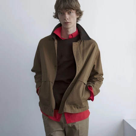 Model Guus Bracke posing in a brown jacket layered over a bright red collared shirt against a white backdrop.