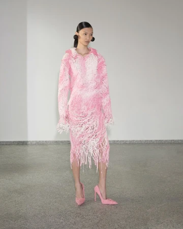 Model wearing a textured pink and white fringed long-sleeve dress and matching pink pointed-toe stiletto heels in a studio.