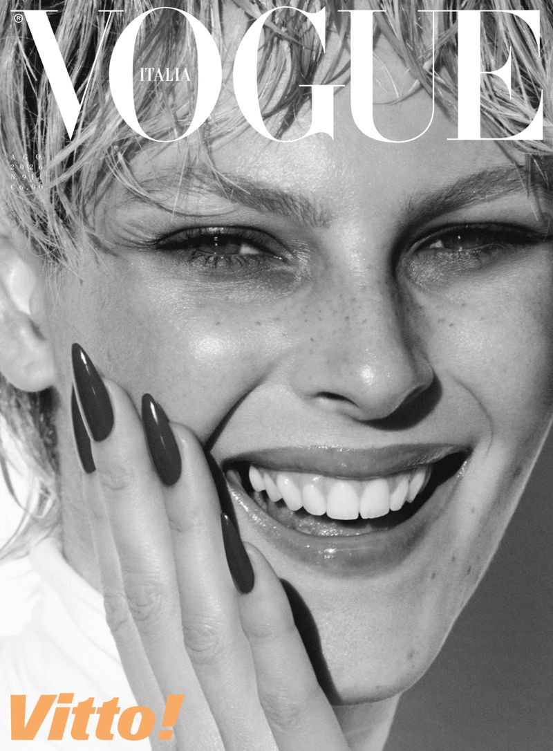 Close-up of a smiling blonde woman with short hair, freckles, and long dark manicured nails touching her cheek on a magazine cover.