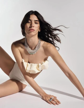 An adult female fashion model poses on a white background, wearing jewelry and a ruffle-trimmed strapless top.