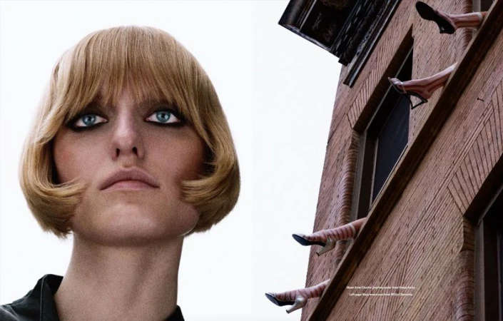 Low-angle portrait of model Maja Slawinska with a short blonde bob beside a brick building featuring legs dangling from windows.