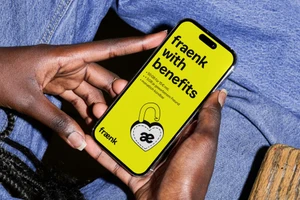 Black hands holding a smartphone showing the fraenk with benefits campaign graphic on a bright yellow screen over blue denim.