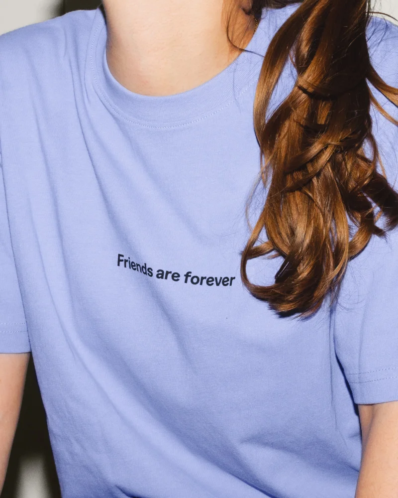 Model wearing a lavender crewneck t-shirt printed with Friends are forever text across the chest.