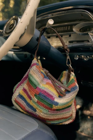 Colorful crocheted stripe handbag hanging from a vintage car steering column inside a classic automobile interior.